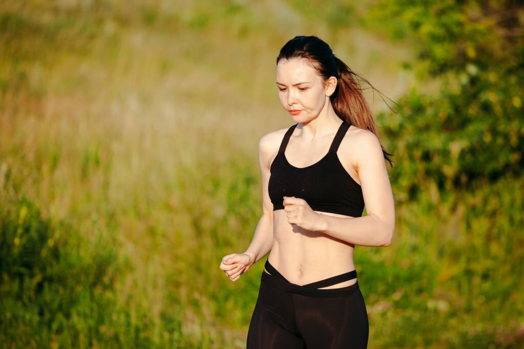 young sports woman engaged in the summer morning running in the Park. in the headphones listening to music from your phone. concept of a healthy lifestyle